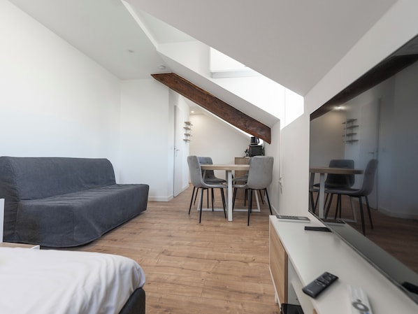 Een moderne, compacte kamer met een bank, een eettafel met stoelen, een grote spiegel en een houten balk in het plafond.