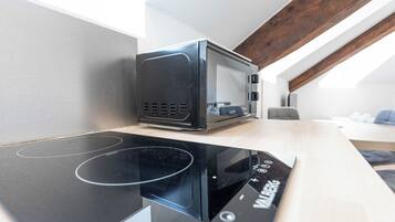 A modern kitchen with a built-in microwave and induction cooktop, a wooden ceiling beam, and a view of a living area.