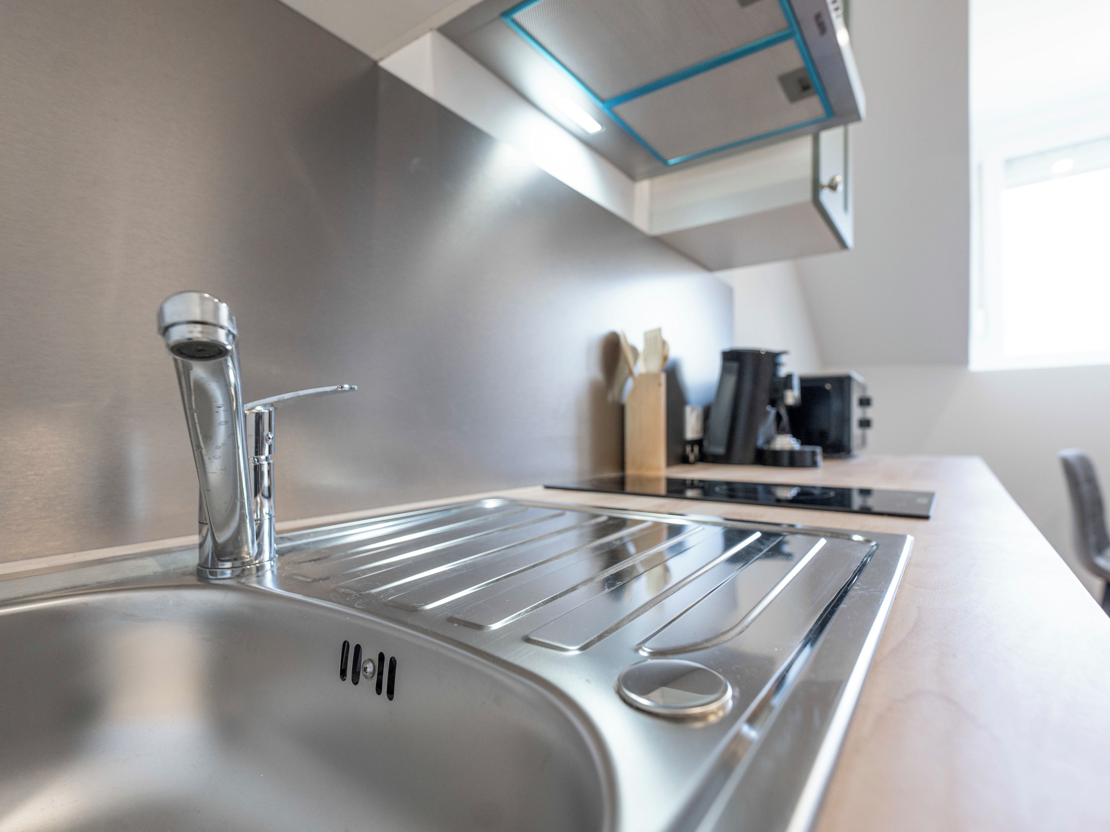 A modern kitchen with a stainless steel sink, a range hood, and a countertop with a coffee maker and utensils.