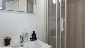 Un baño con un lavamanos blanco, un espejo, una cabina de ducha de vidrio y una toalla en el suelo.