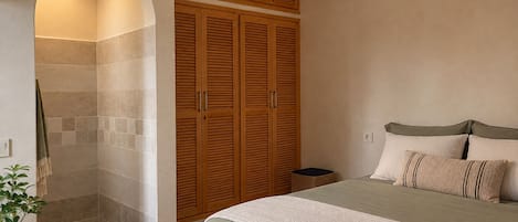 A bedroom with a bed, a wooden wardrobe, and a shower area.