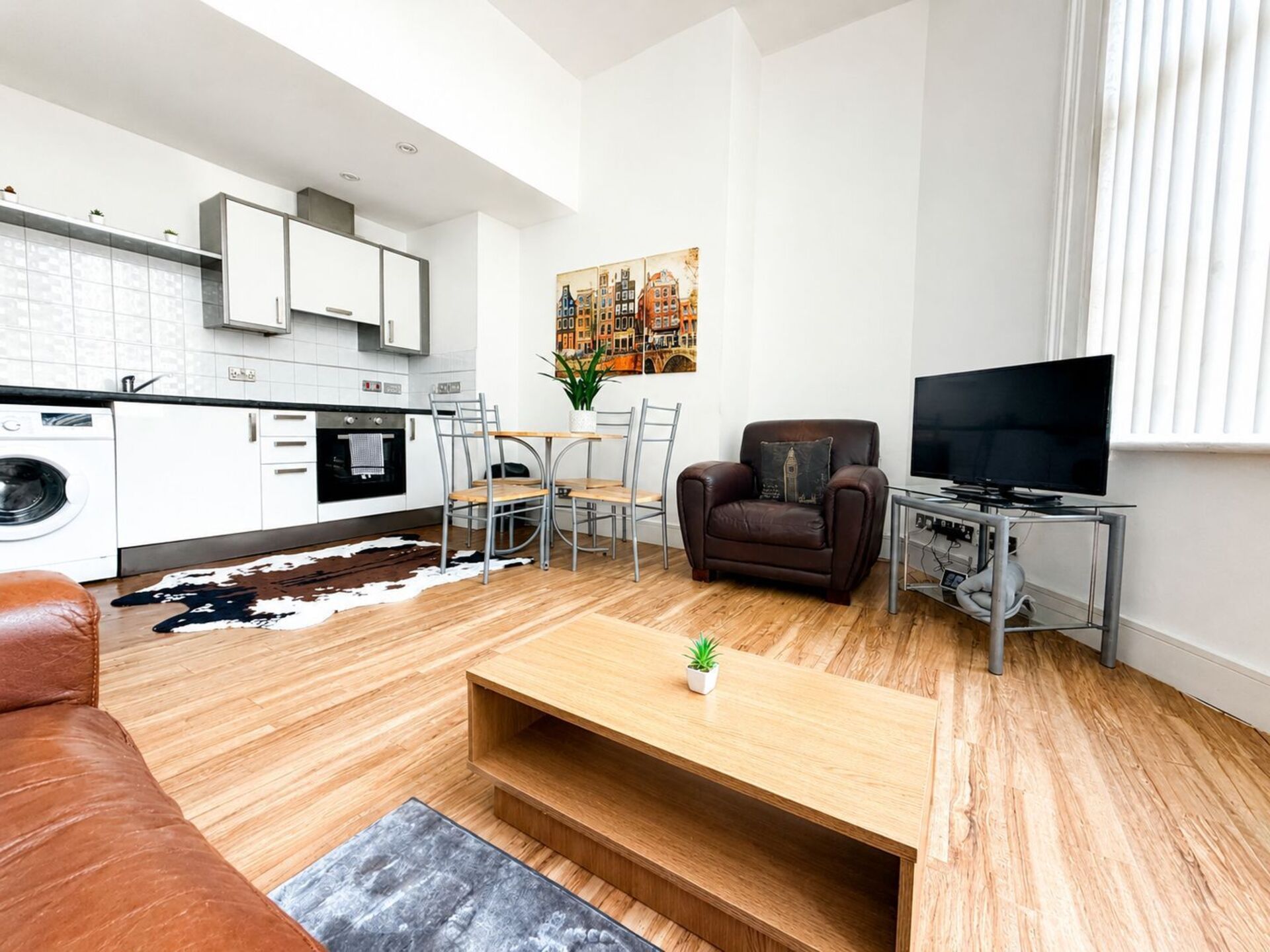 A modern living room with a sofa, a coffee table, a TV, and a dining area with chairs and a table.