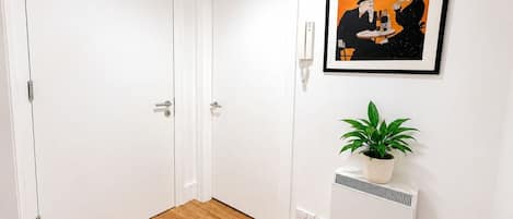 Un pasillo con puertas blancas, un cartel enmarcado y una planta en maceta sobre un radiador.