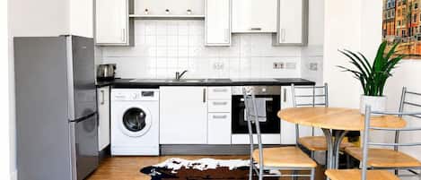 Eine kompakte Küche mit weißen Schränken, einer Waschmaschine, einem Kühlschrank und einem Essbereich mit Tisch und Stühlen.