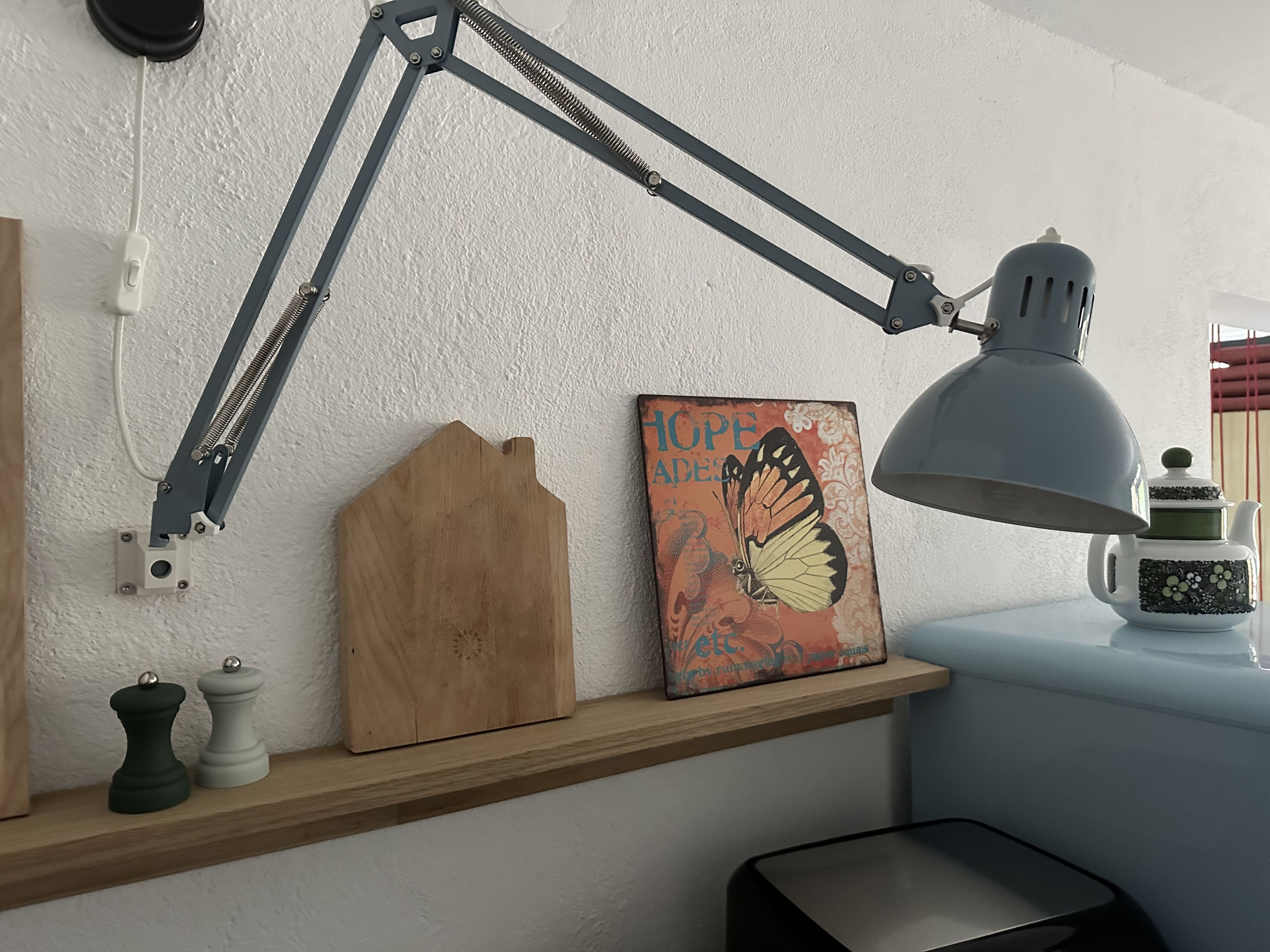 A desk with a desk lamp, a wooden board, a decorative plate, and a wall-mounted light switch.