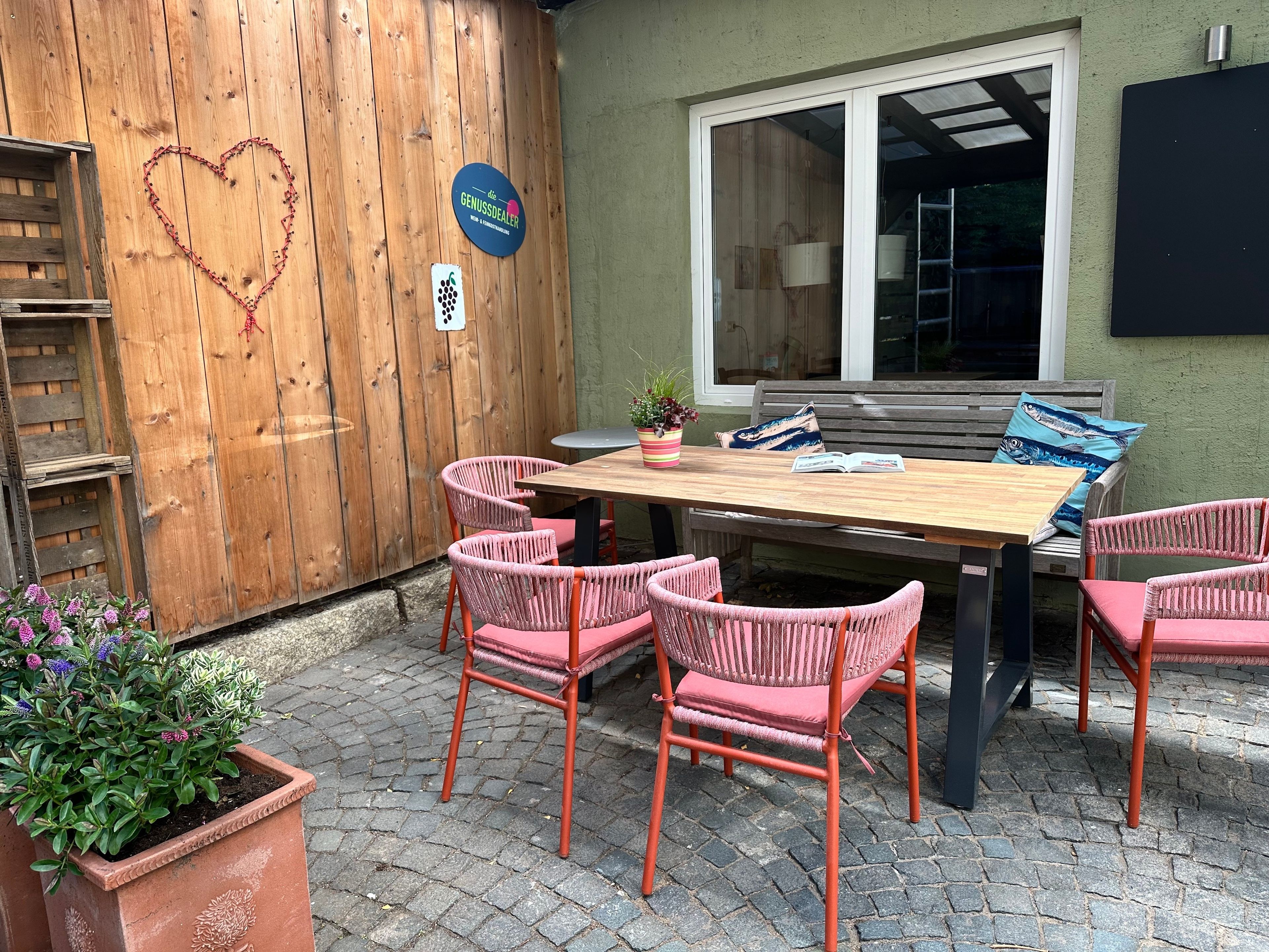 Eine Terrasse im Freien mit einem Holztisch, Korbstühlen und einer Bank.