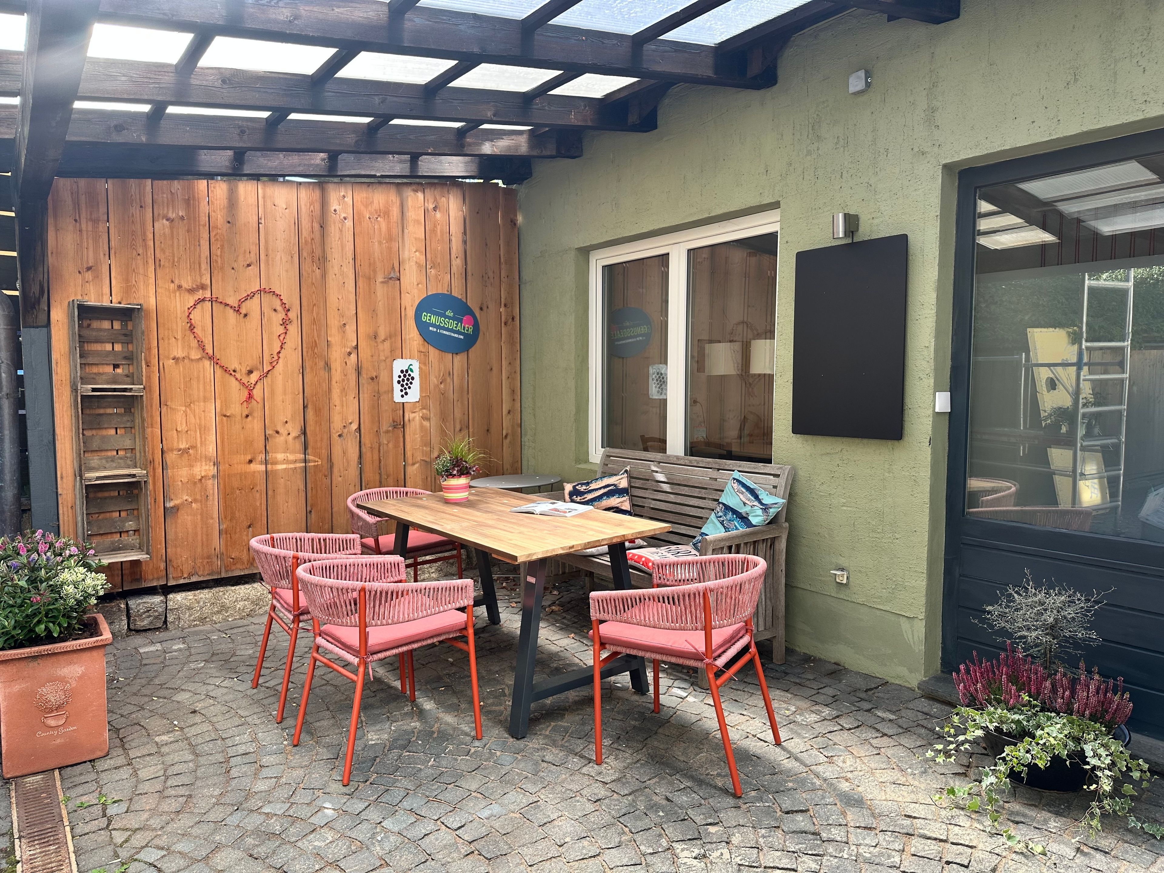Un patio al aire libre con una mesa y sillas de madera, un banco y plantas en macetas.