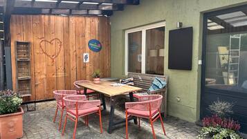 Un patio al aire libre con una mesa y sillas de madera, un banco y plantas en macetas.