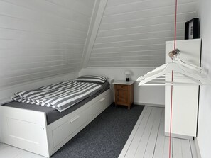 A bedroom with a bed, a nightstand, a dresser, and a hanging light fixture.