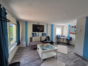 Ein kompakter Wohnbereich mit einer Couch, einem Glastisch, einer kleinen Essecke und einem Fenster mit Vorhängen.