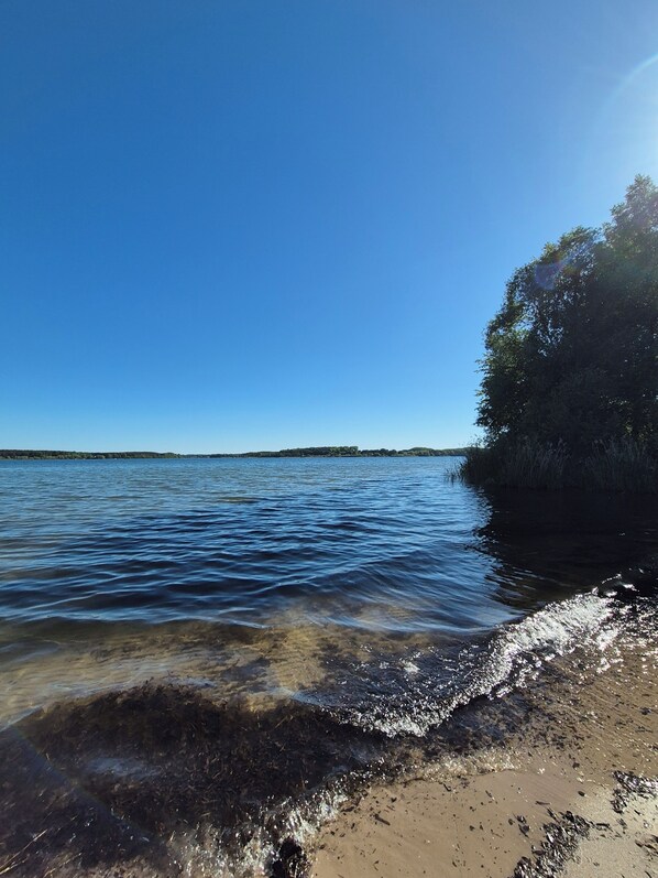 Ein Strand mit klarem Wasser, sandigem Ufer und einer entfernten Küste.
