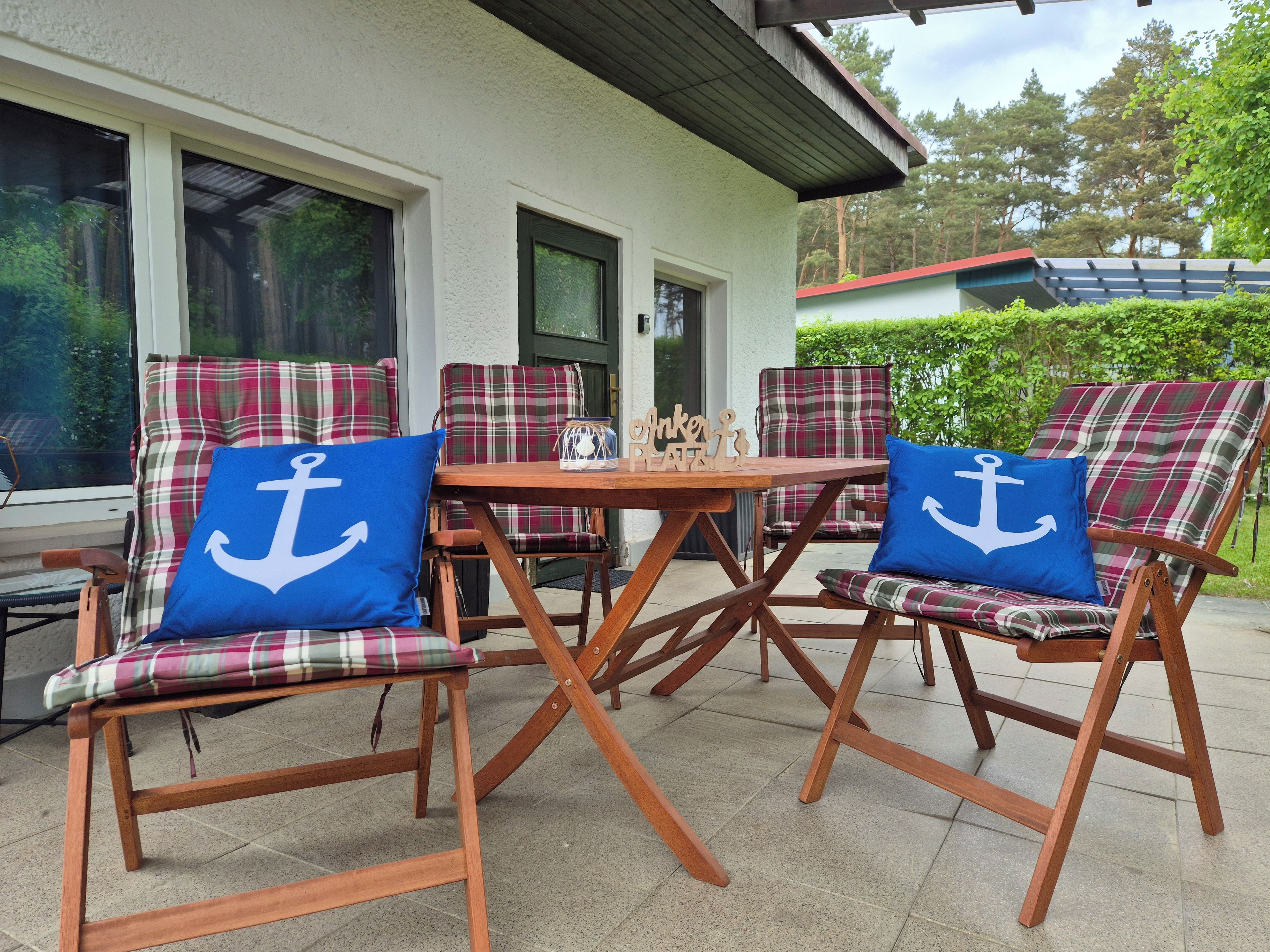 An outdoor seating area with plaid chairs and blue pillows, a wooden table, and a view of a building with large windows.