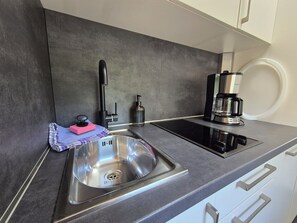 Eine moderne Küche mit Spüle aus Edelstahl, einer Kaffeemaschine und einem integrierten Induktionskochfeld.