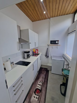 A compact kitchen with white cabinetry, a black induction cooktop, a coffee maker, and a mini fridge. - Bright, Modern 3-Room Apartment Near Munich Airport, S-Bahn, 30 Min to City Center (Neufahrn bei Freising)