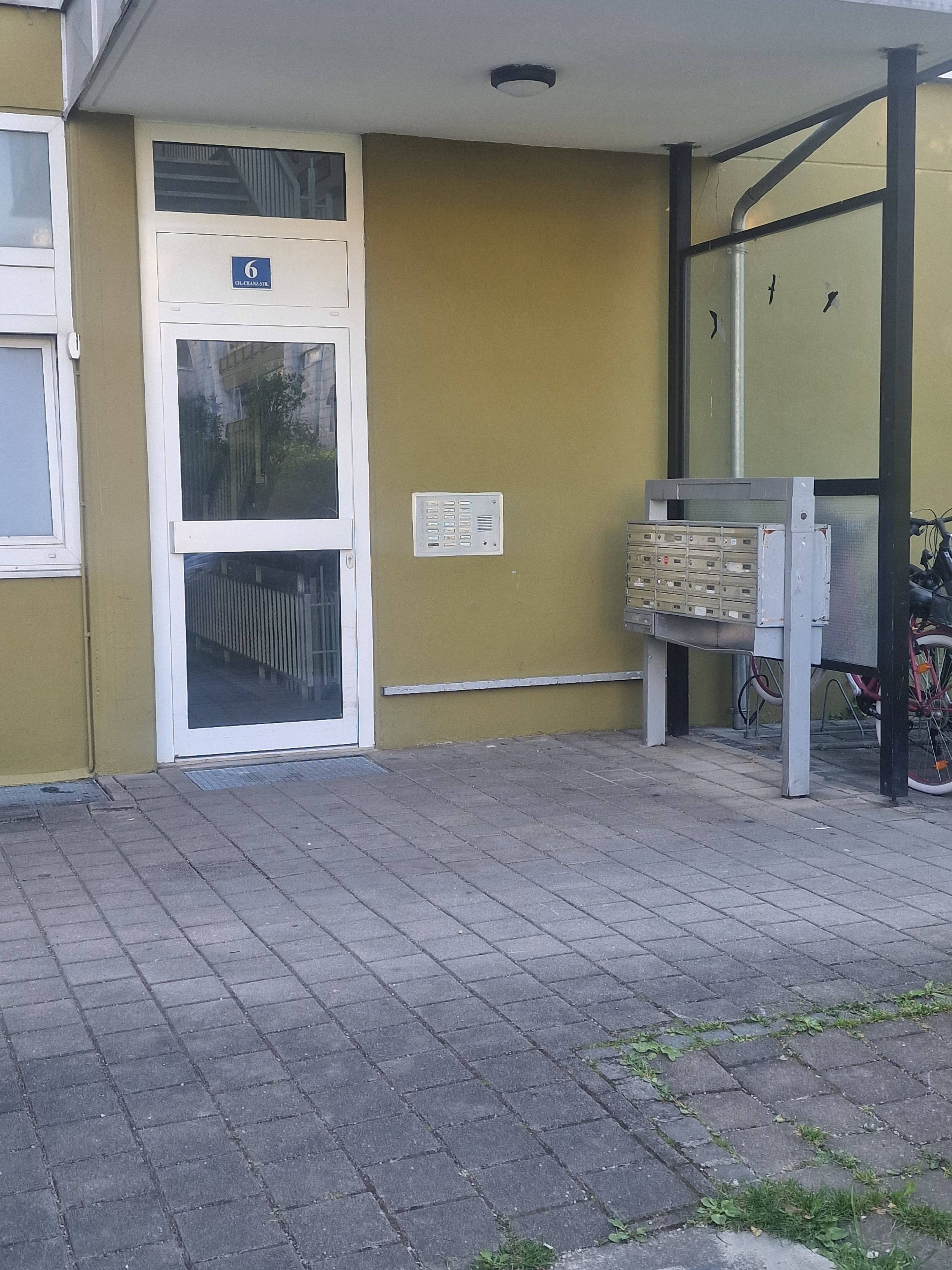 Ein Gebäudeeingang mit einer Tür, auf der die Zahl 6 steht, und einem Fahrrad davor.
