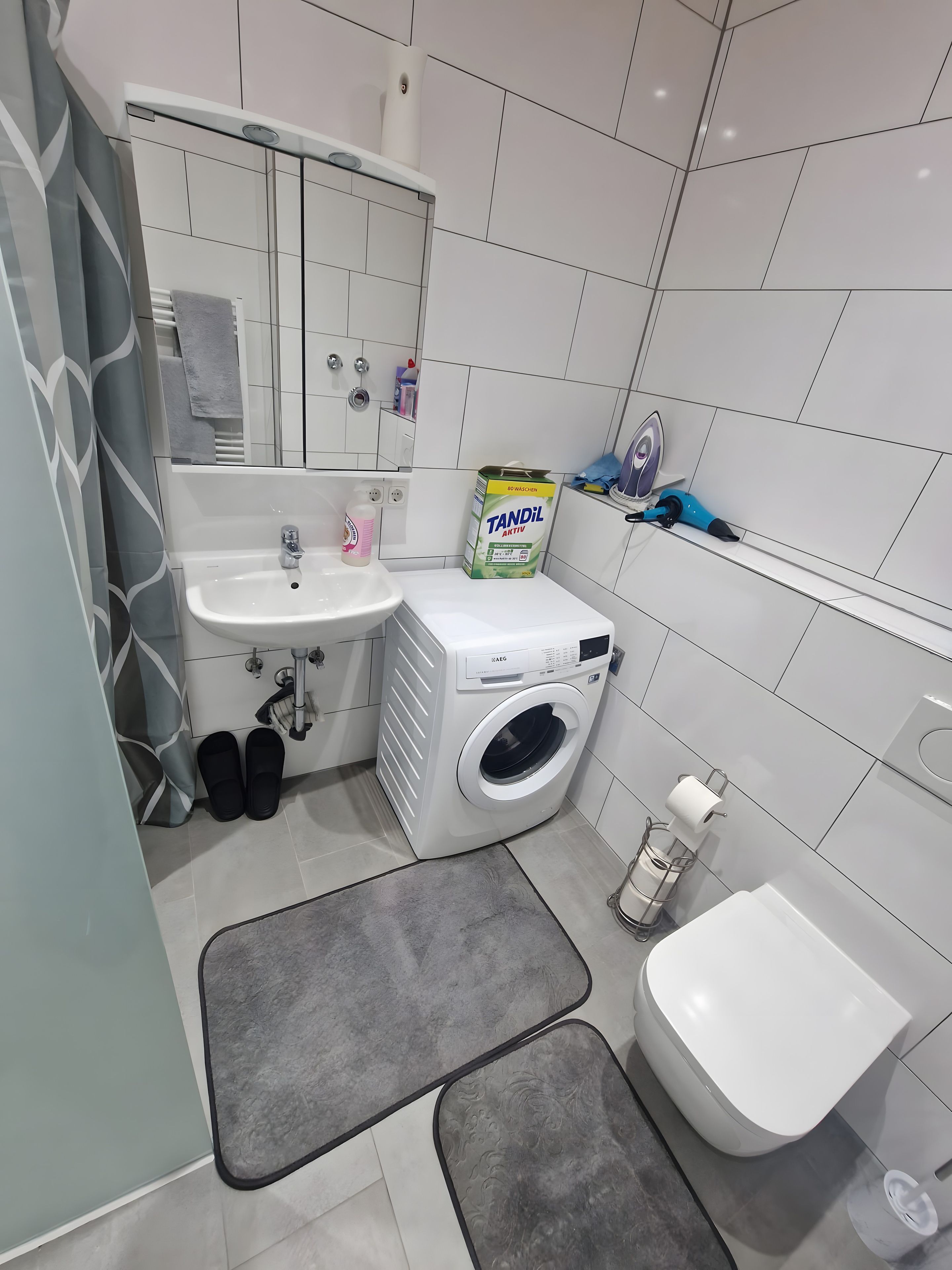 Un baño moderno con lavamanos, lavadora, inodoro y zona de ducha.