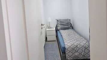A small, modern bedroom with a single bed, a bedside table with a lamp, and a grey rug.