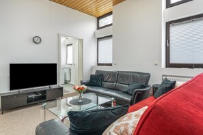 Sala de estar moderna com televisão de tela plana, sofá de couro, mesa de centro de vidro e um almofado vermelho.