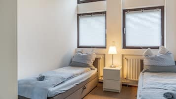 Ein kleines, helles Schlafzimmer mit zwei Einzelbetten, einem Nachttisch mit Lampe und einem Heizkörper.