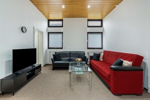 A modern living room with a flat-screen TV, leather sofas, a glass coffee table, and a wooden ceiling.