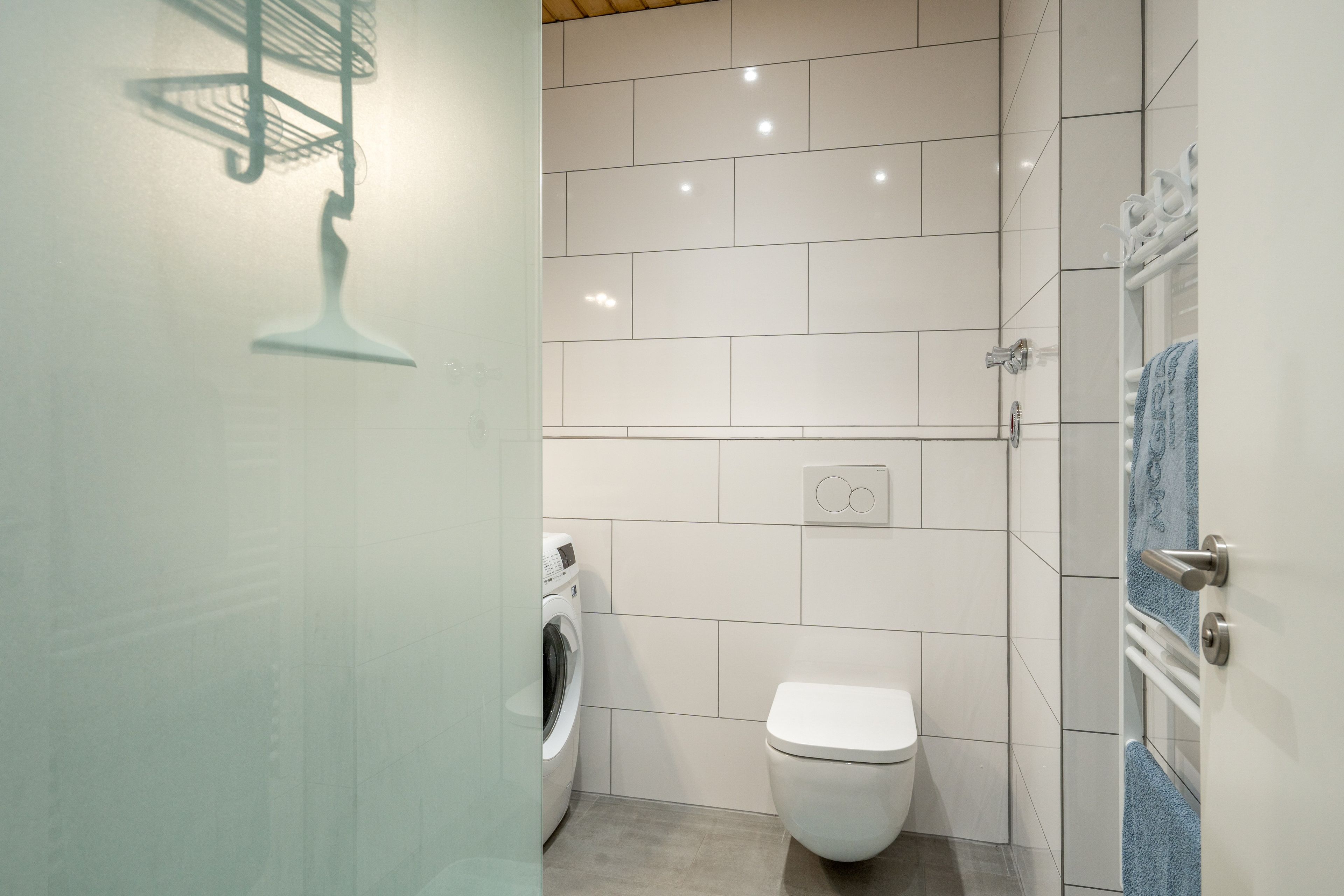 A modern bathroom with a toilet, washing machine, and a towel rack.