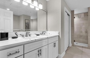 A modern bathroom with a double sink vanity, a large mirror, and a walk-in shower. - 7403 Luxurious  2/2 Resort Condo Near Disney (Orlando)