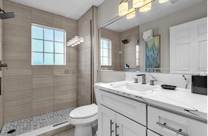 Un baño moderno con ducha, inodoro y tocador con un espejo grande.