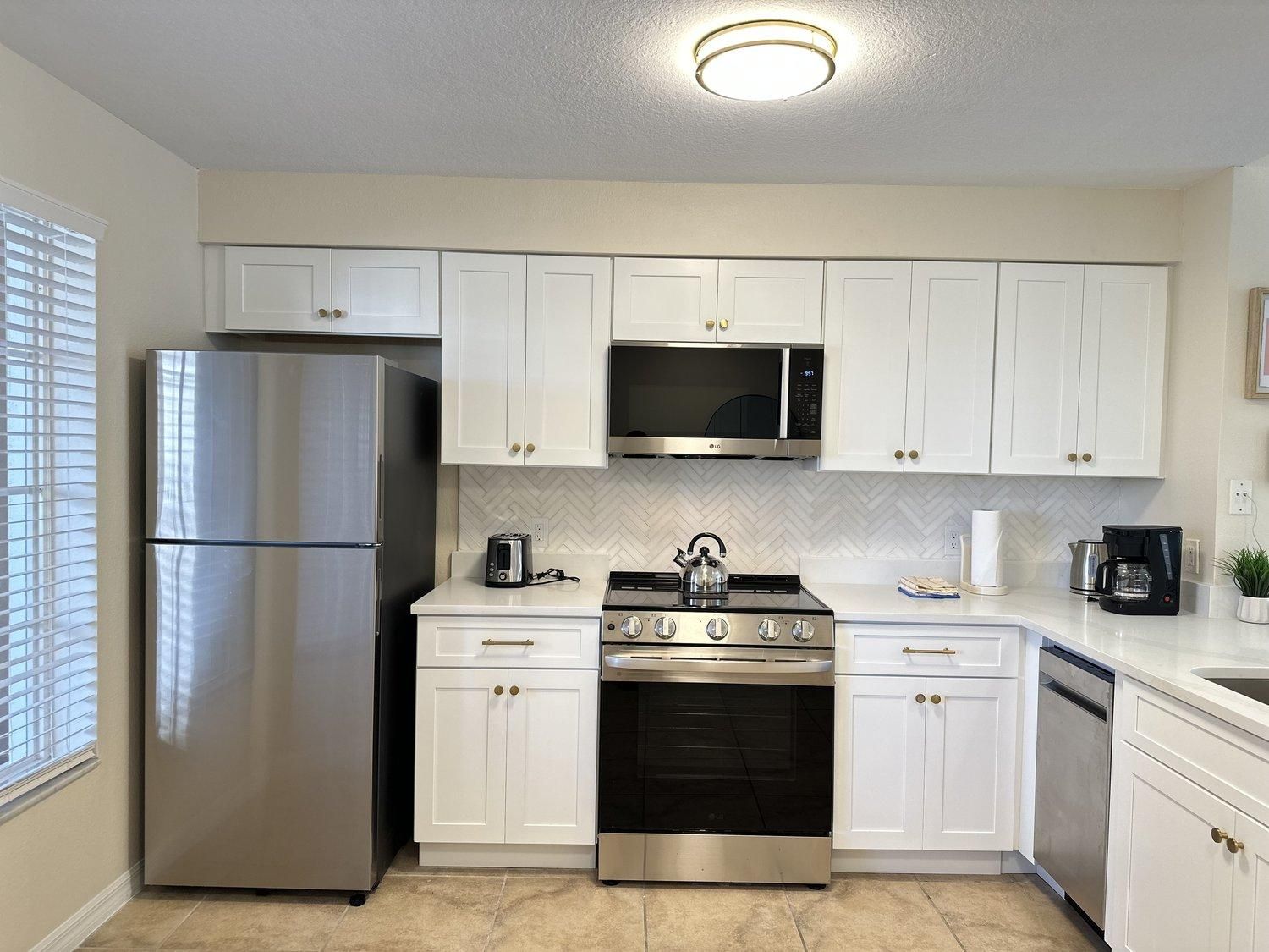 Uma cozinha moderna com eletrodomésticos de aço inoxidável, armários brancos e backsplash de azulejos em padrão herringbone.
