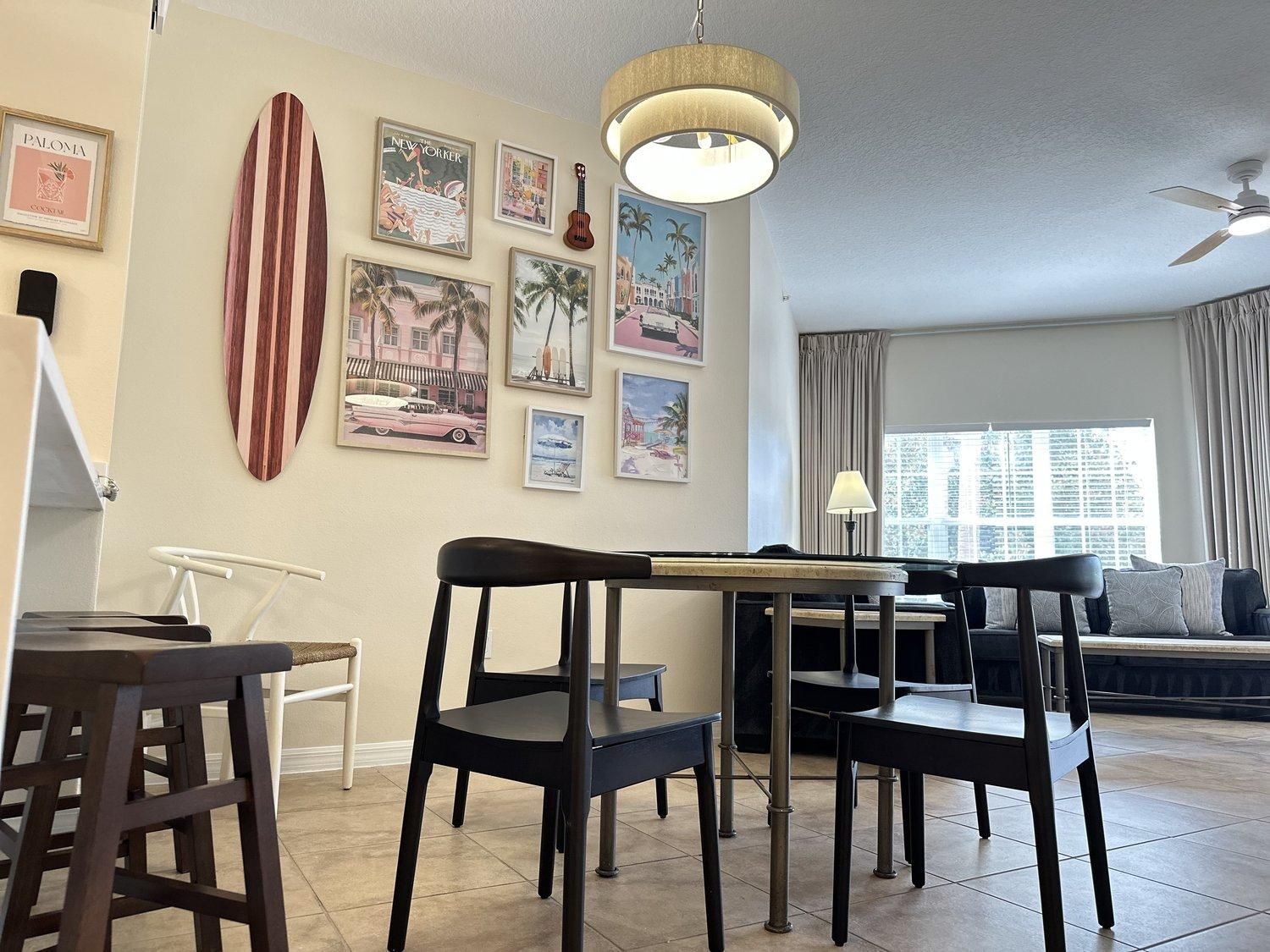 Una sala de estar con comedor, una tabla de surf y varias fotografías enmarcadas en la pared.