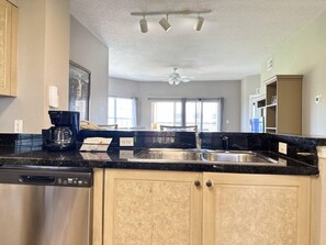 A kitchen with a dishwasher, coffee maker, and a sink. There is a ceiling fan and a window with curtains. - 1406 Spacious 2/2 Resort Condo Near Disney (Orlando)