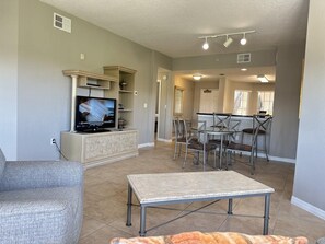 A living room with a television, a dining area with chairs, and a kitchen in the background. - 1406 Spacious 2/2 Resort Condo Near Disney (Orlando)