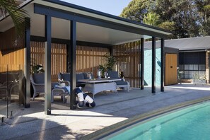A covered outdoor seating area with wicker furniture, a pool, and a wooden fence.