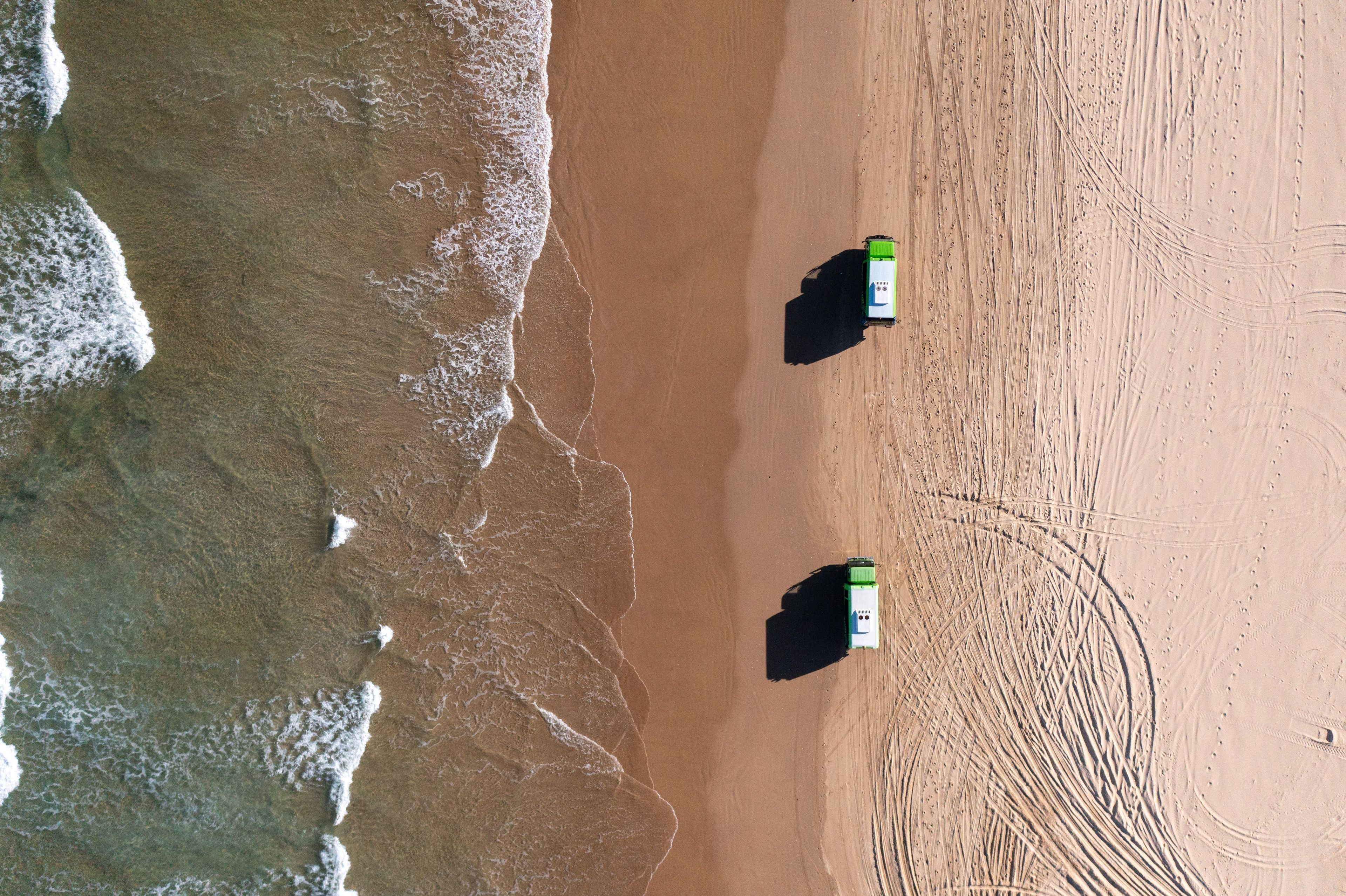 Vista aérea de uma praia com dois barcos verdes e brancos estacionados na areia.