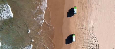 Vista aerea di una spiaggia con due barche verde e bianche ormeggiate sulla sabbia.