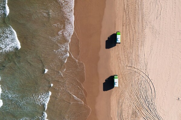 An aerial view of a beach with two green and white boats parked on the sand.