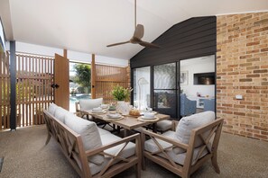An outdoor dining area with a table set for two, wooden chairs, and a ceiling fan.