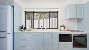 Una cocina con armarios azul claro, una ventana con vista a árboles, un horno empotrado y una cafetera.