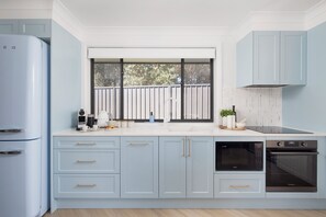 A kitchen with light blue cabinets, a window with a view of trees, a built-in oven, and a coffee maker.