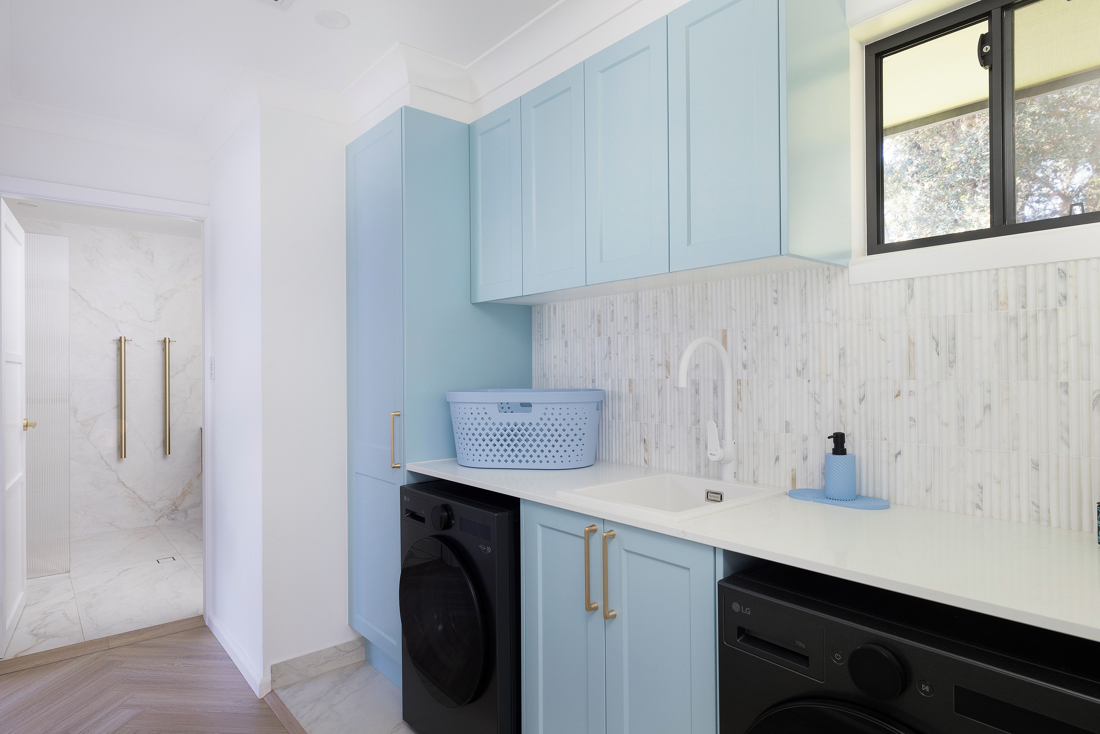 A modern kitchen with light blue cabinets, a white countertop, and a black washing machine.