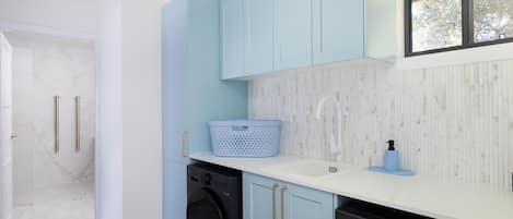 A modern kitchen with light blue cabinets, a white countertop, and a black washing machine.