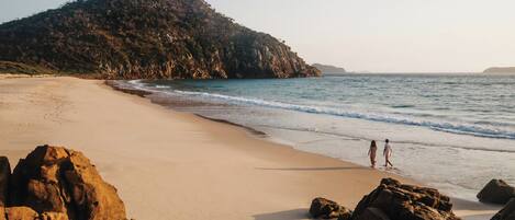 A beach with rocky formations and a large hill in the background.