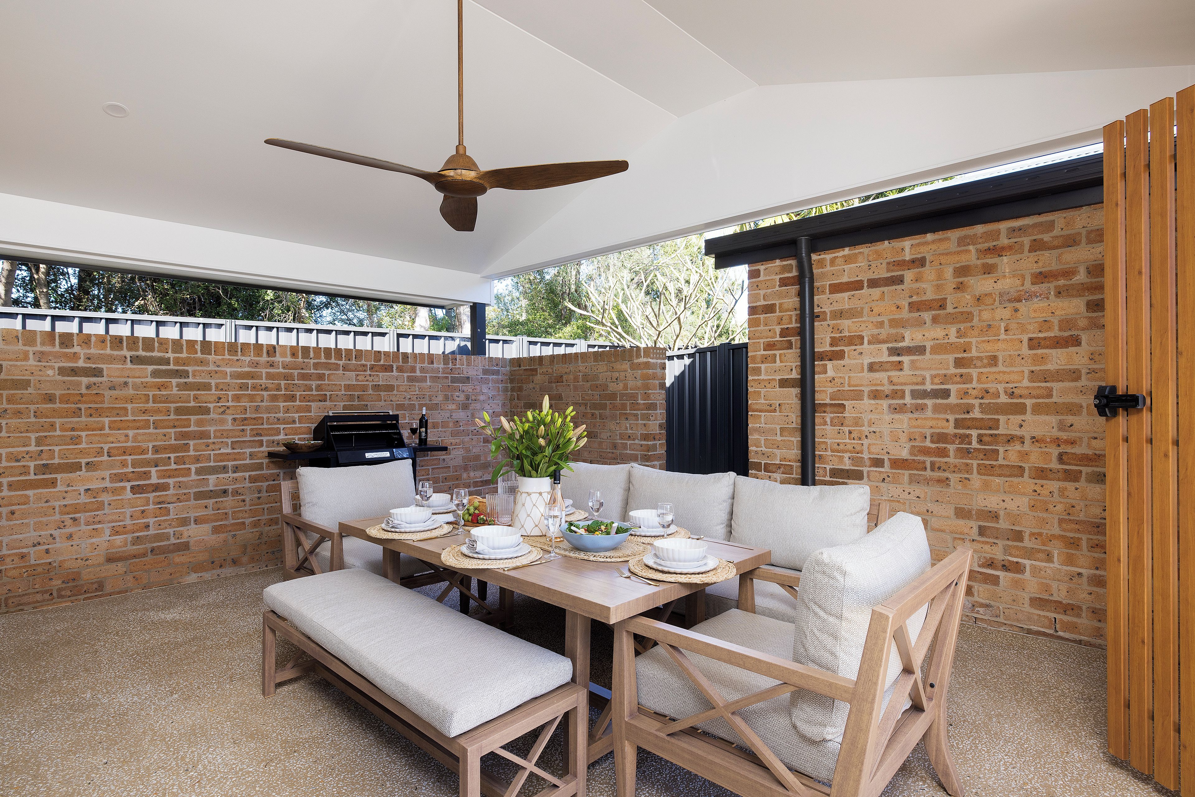 An outdoor dining area with a brick wall, a ceiling fan, and a table set for two.