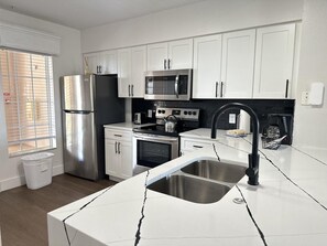 A modern kitchen with white cabinetry, stainless steel appliances, and a black faucet. - 1506 Luxurious 2/2 Resort Condo Near Disney (Orlando)