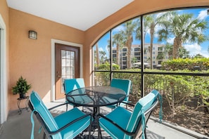 A balcony with a round table and chairs, a door, and a view of palm trees and buildings. - 2103 Spacious 2/2 Resort Condo Near Disney (Orlando)