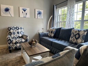 A living room with a patterned armchair, a sofa with patterned cushions, a wooden coffee table, and wall art. - 2206 Spacious 2/2 Resort Condo Near Disney (Orlando)