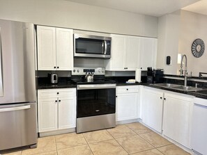 A modern kitchen with white cabinets, stainless steel appliances, a microwave, and a kettle. - 2206 Spacious 2/2 Resort Condo Near Disney (Orlando)