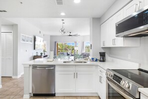 A modern kitchen with white cabinetry, stainless steel appliances, and a central island with seating. - 2303 Spacious 2/2 Resort Condo Near Disney (Orlando)