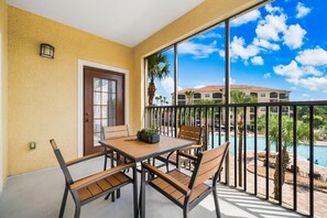 A balcony with a table and chairs, a door, and a view of a swimming pool and buildings. - 2303 Spacious 2/2 Resort Condo Near Disney (Orlando)