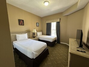 A hotel room with two beds, a desk with a TV, a window with curtains, and a lamp. - 2306 Spacious 2/2 Resort Condo Near Disney (Orlando)