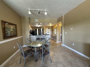 A dining area with a round glass table and metal chairs, a kitchen in the background, and a hallway leading to other rooms. - 2403 Spacious 2/2 Resort Condo Near Disney (Orlando)
